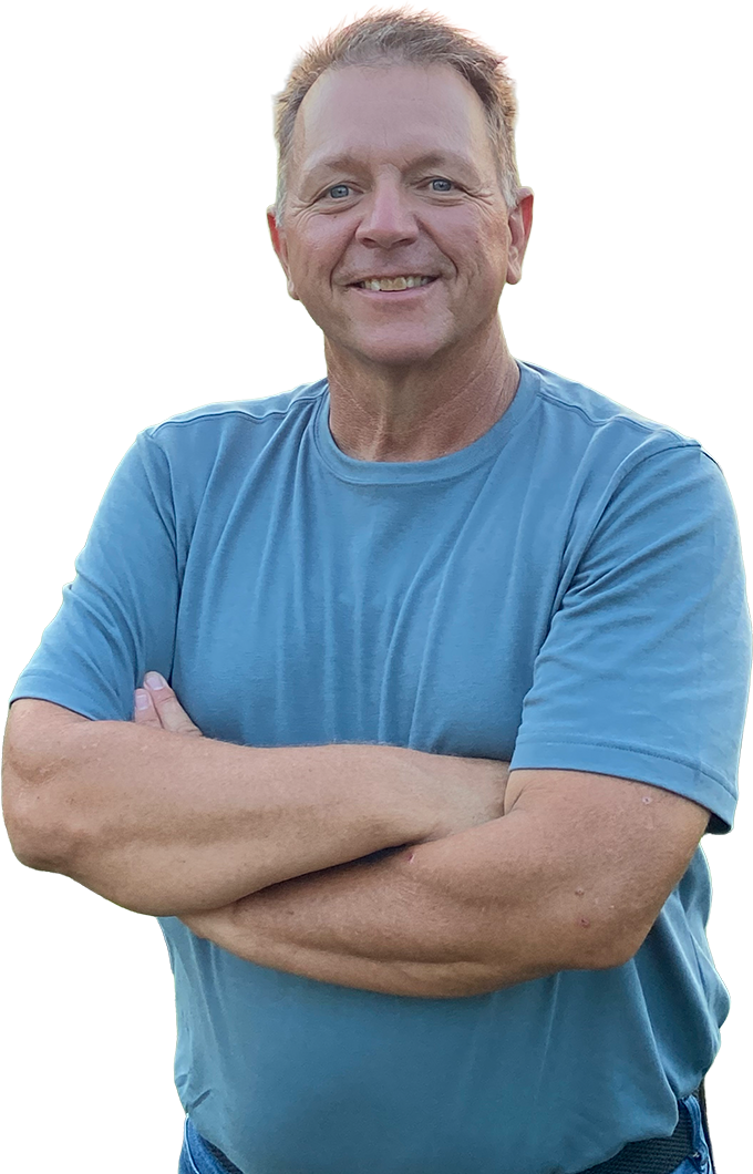 Daryl Schmitt standing smiling in front of a field of greenery on a farm during sunrise